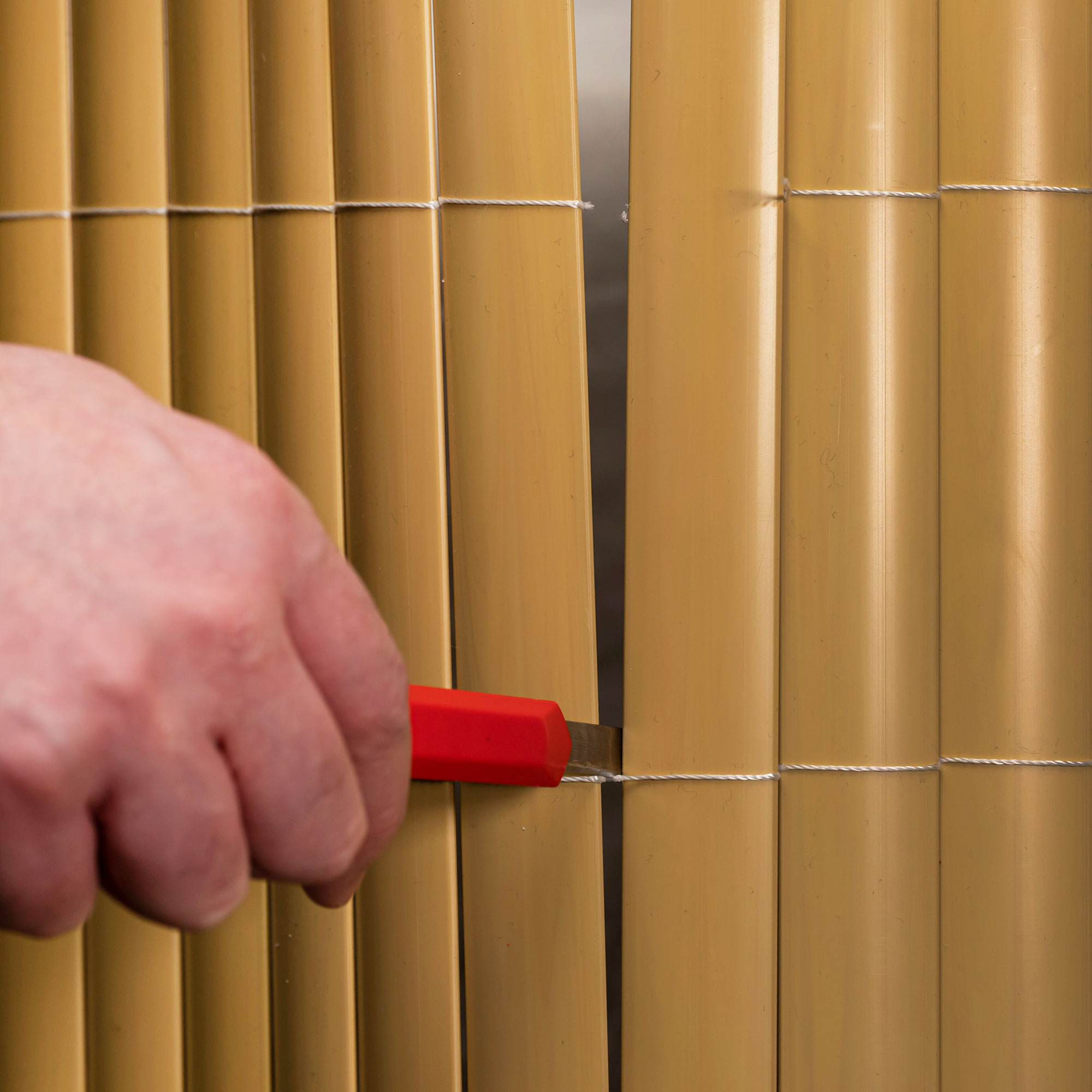 Mano che taglia una rete di protezione in PVC con un coltello, mostra il montaggio o l'adattamento del materiale