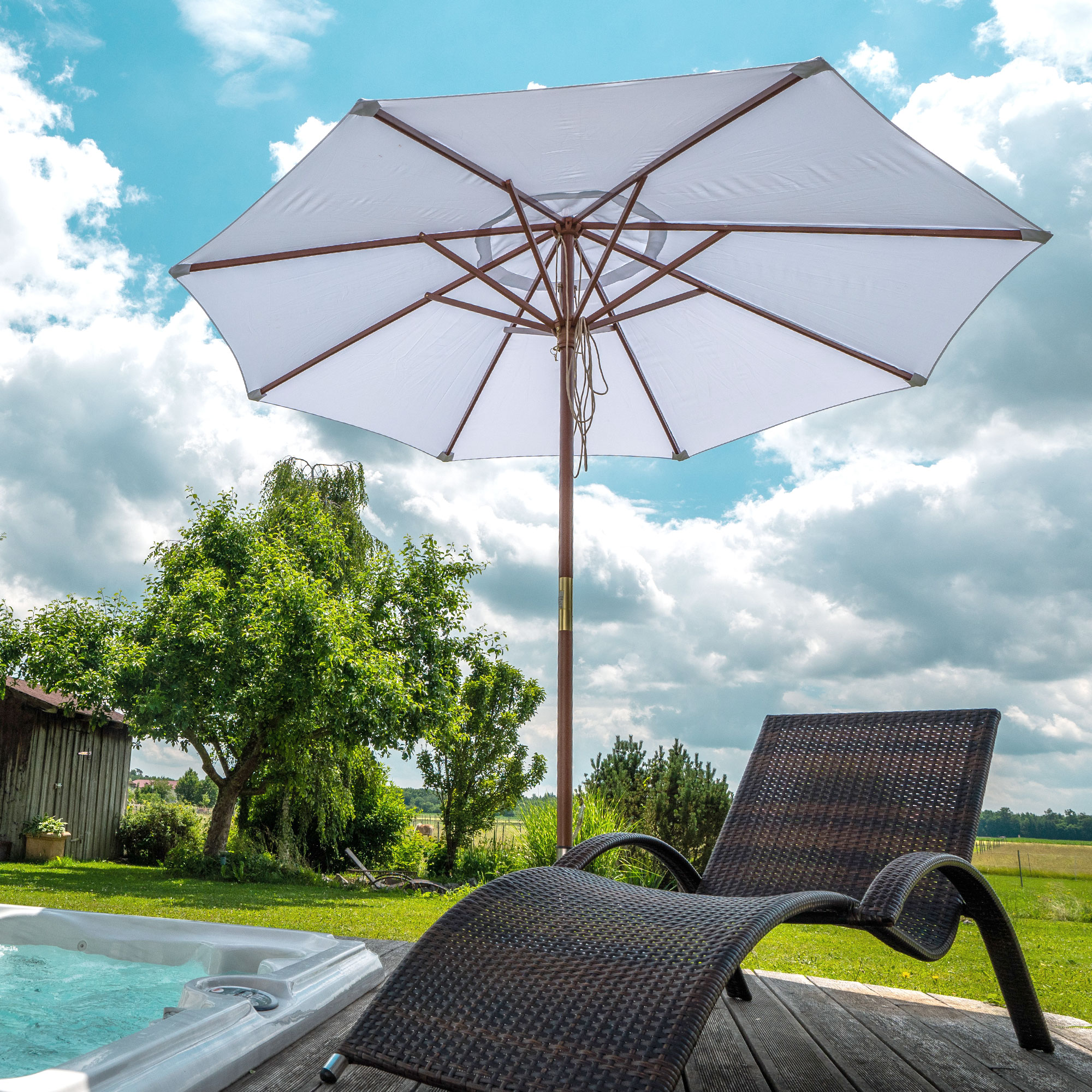 Ombrellone con struttura in legno nel giardino accanto a una sdraio e a una piscina