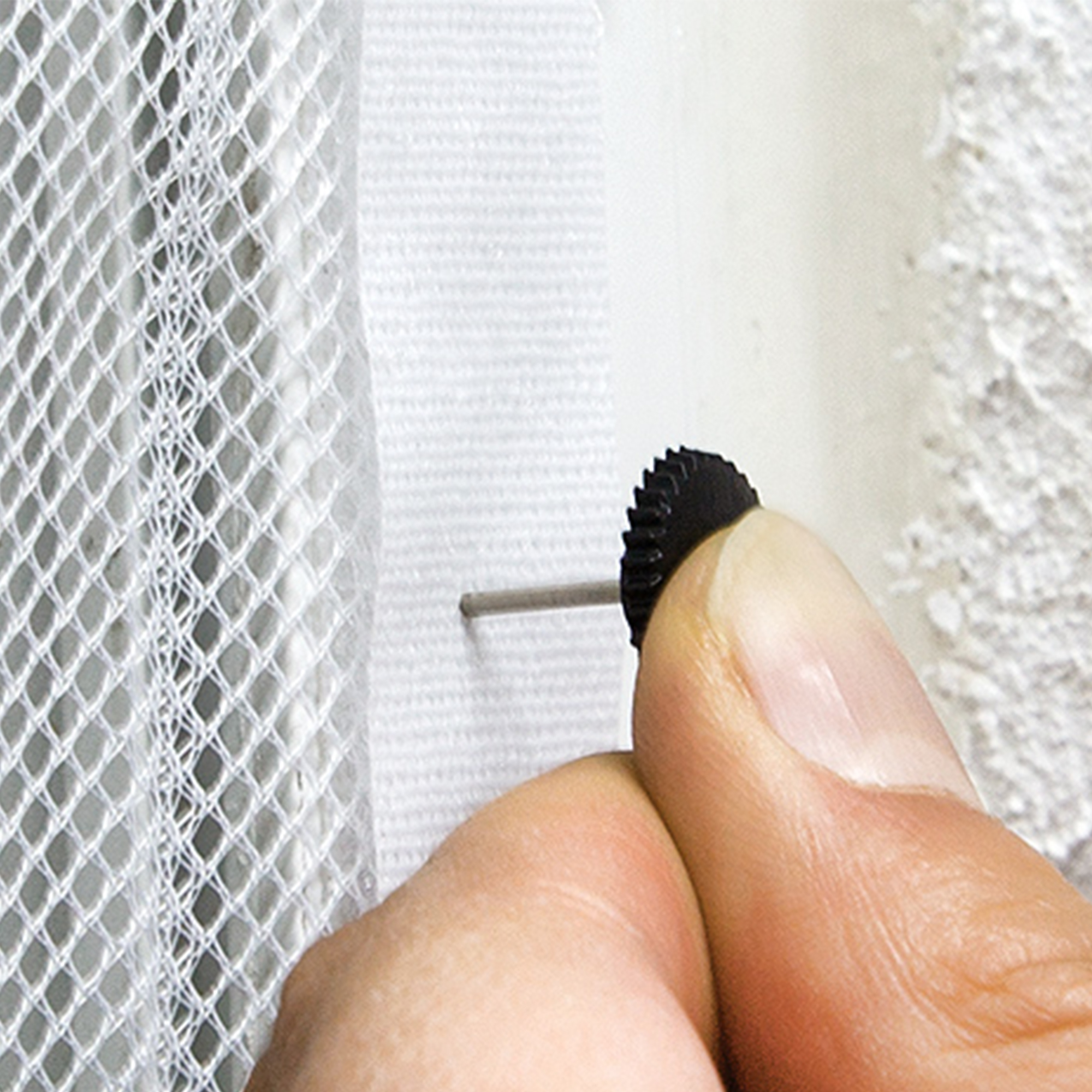 Mano che fissa un tessuto a rete con un piccolo chiodo a una superficie murale