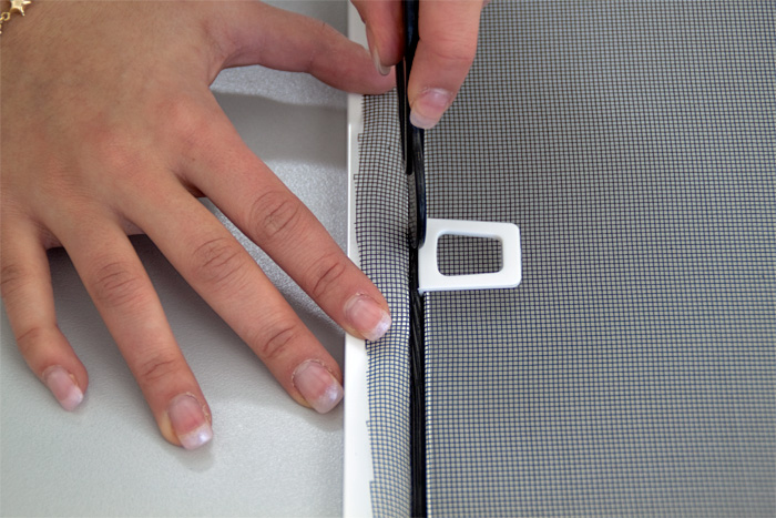 Mani usano lo strumento in PVC per fissare la protezione contro gli insetti nel telaio